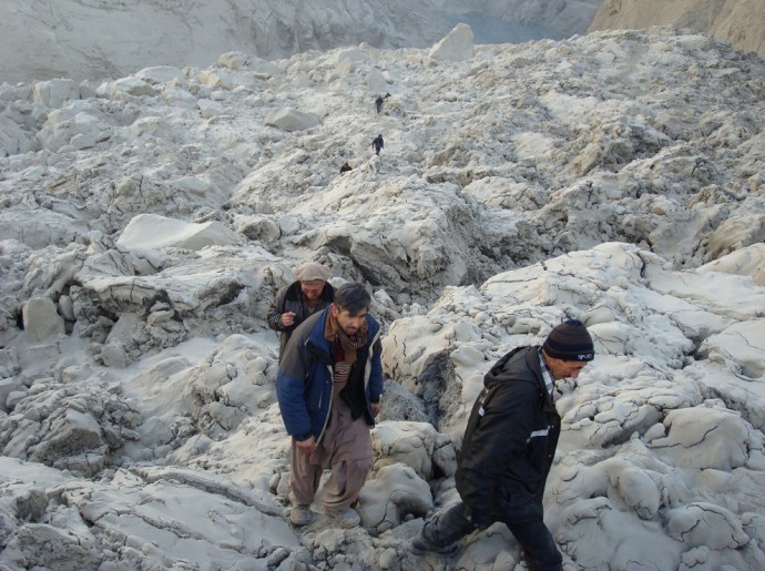 Люди проходят по завалам, образовавшимся после оползня, долина реки Хунза. На заднем плане виднеется озеро, уровень воды в котором быстро поднимается: